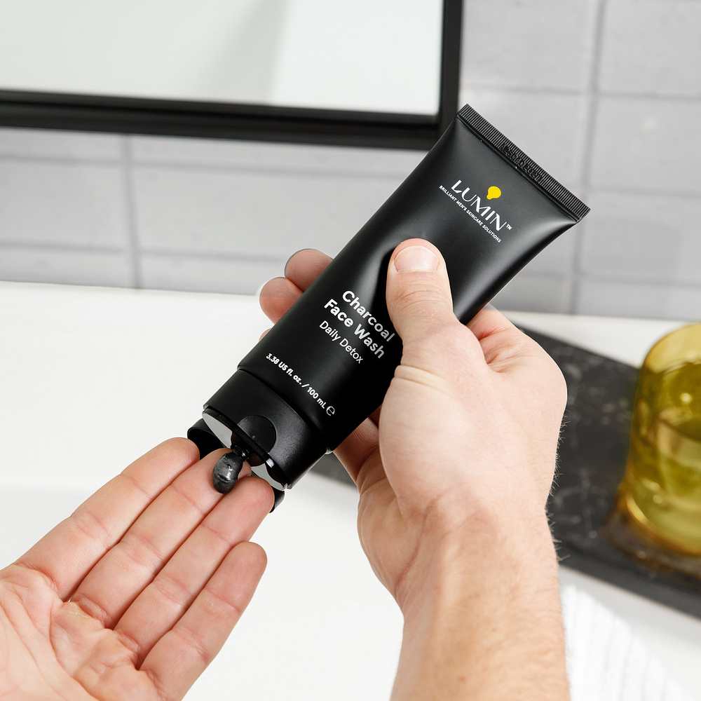 Lumin Charcoal Face Wash Daily Detox being dispensed from black tube onto hand in modern bathroom setting