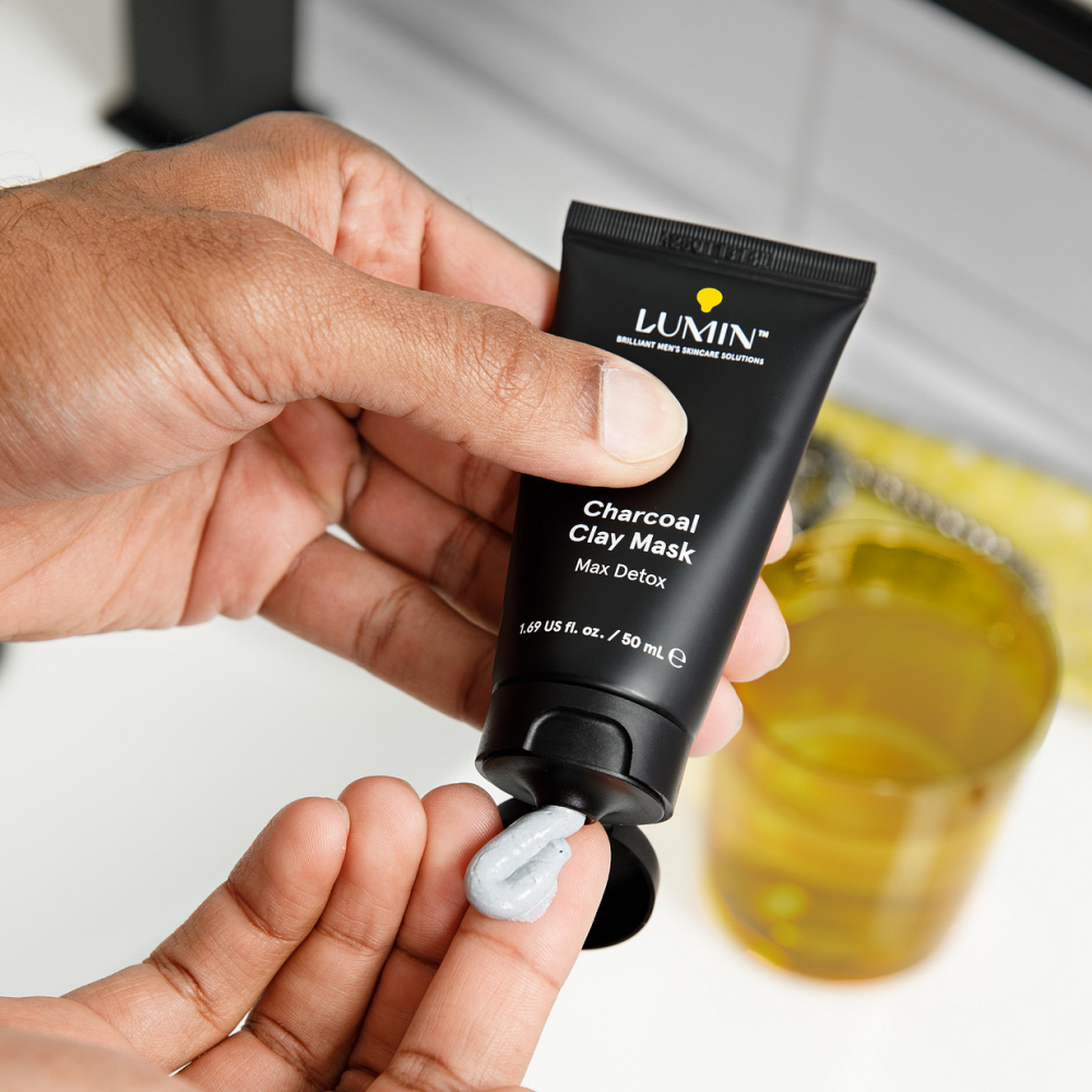 Hand applying Lumin charcoal clay mask skincare cream from black tube for men's deep detox and cleansing routine.