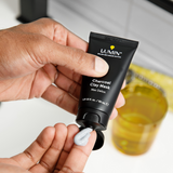 Hand applying Lumin charcoal clay mask skincare cream from black tube for men's deep detox and cleansing routine.