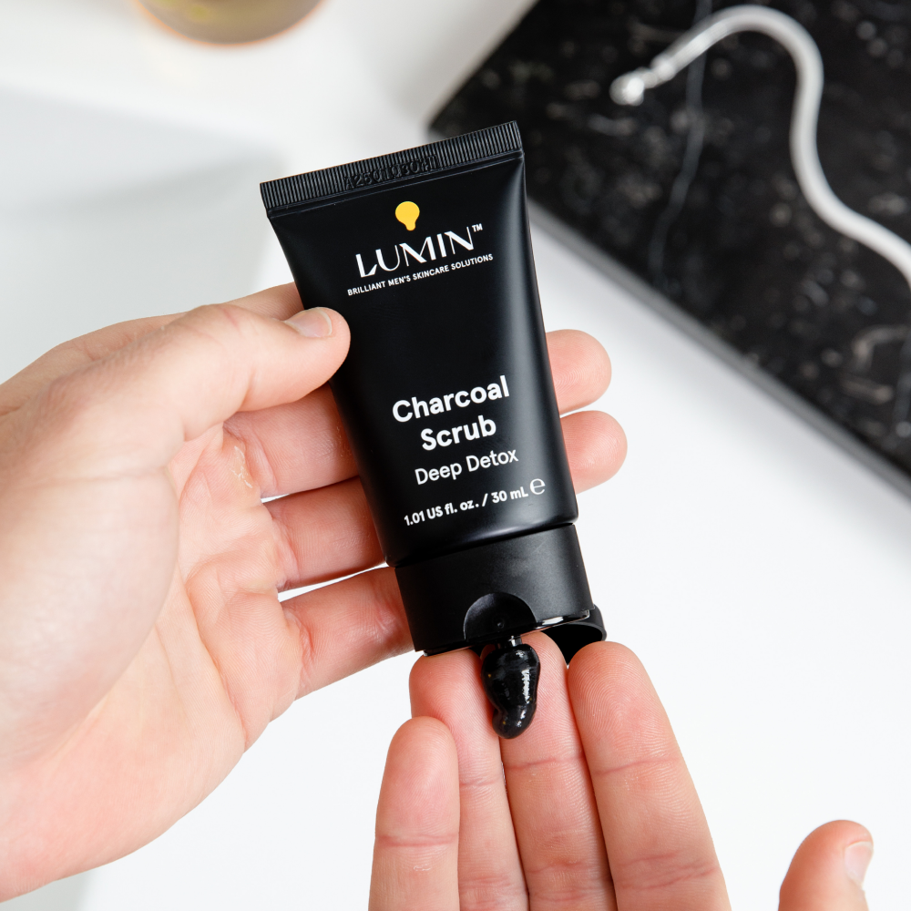 Lumin Charcoal Scrub tube with black detox scrub on fingertips, men's skincare, deep cleansing exfoliating face scrub.