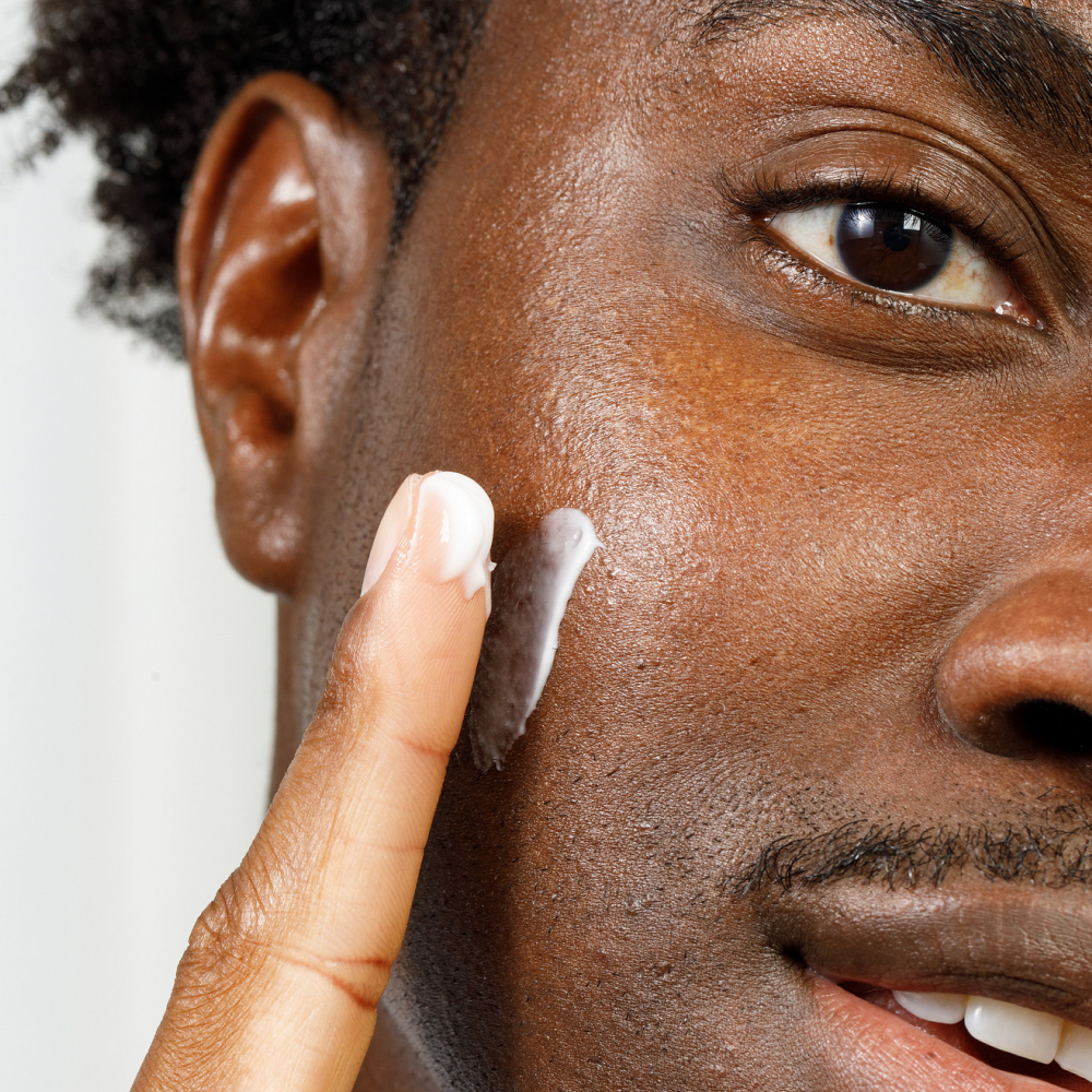Moisturizing cream being applied on dark skin close-up, highlighting skincare routine and healthy complexion.