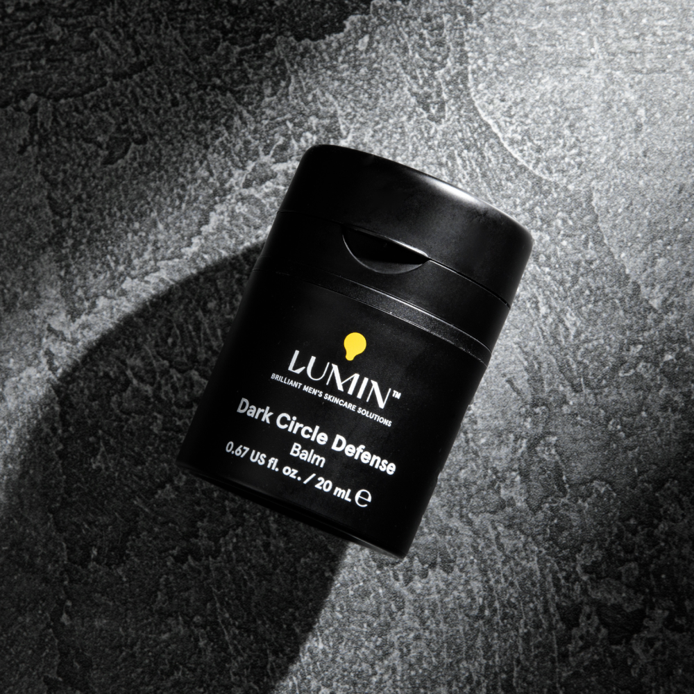 Lumin Dark Circle Defense Balm in black container on textured dark stone surface, men's skincare for eye care.