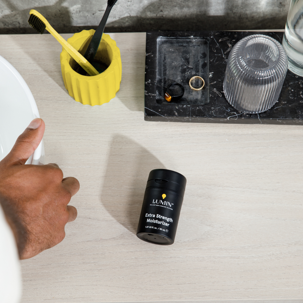 Lumin Extra Strength Moisturizer bottle on light wood bathroom counter with toothbrush holder and ring tray.