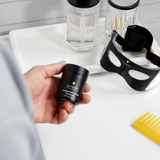 Hand holding Lumin Instant Dark Circle Corrector next to black light therapy eye mask, clear skincare bottles, and yellow comb on white surface