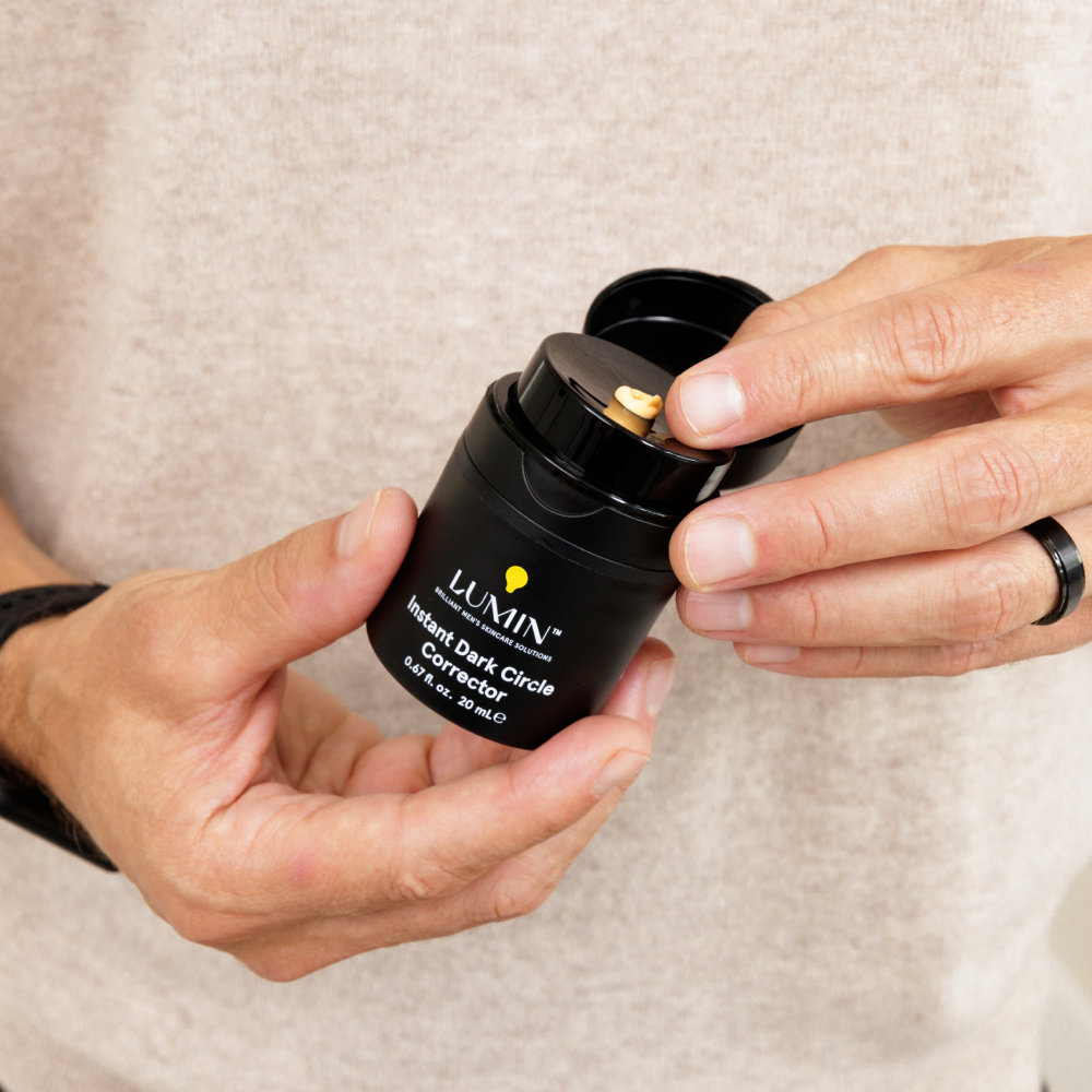 Lumin Instant Dark Circle Corrector cream in black container being dispensed on finger, men's skincare product.