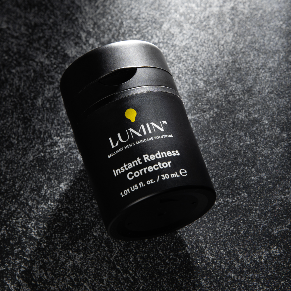 Lumin Instant Redness Corrector black skincare bottle on textured dark surface for men’s skincare.