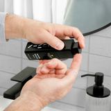 Hands dispensing black Lumin wrinkle defense serum bottle over bathroom sink with black faucet and soap dispenser.
