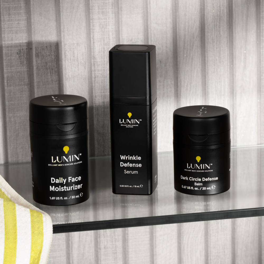 Lumin men's skincare trio with Daily Face Moisturizer, Wrinkle Defense Serum, and Dark Circle Defense Balm on glass shelf