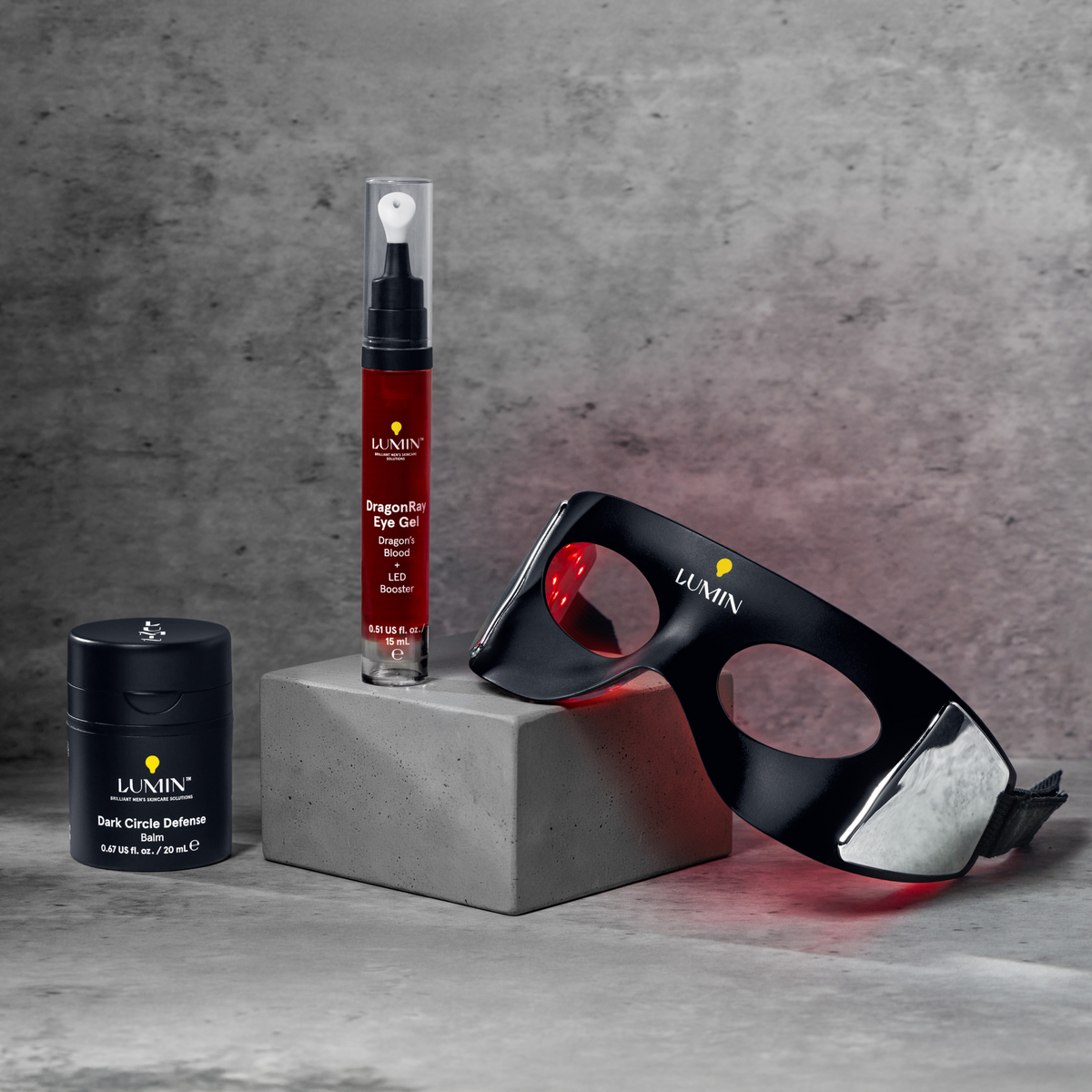 Luxury skincare set featuring anti-aging cream, serum in red bottle, and black LED therapy eye mask on gray background