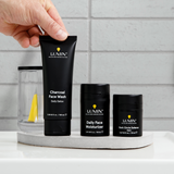 Lumin men's skincare set with charcoal face wash, daily moisturizer, and dark circle defense balm on a white marble tray.