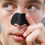 Close-up of man applying black charcoal nose strip for blackhead removal and skincare treatment