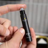 Lumin Recovery Oil skincare roller with moisturizing oil on fingertip, black travel-size bottle, men's grooming product