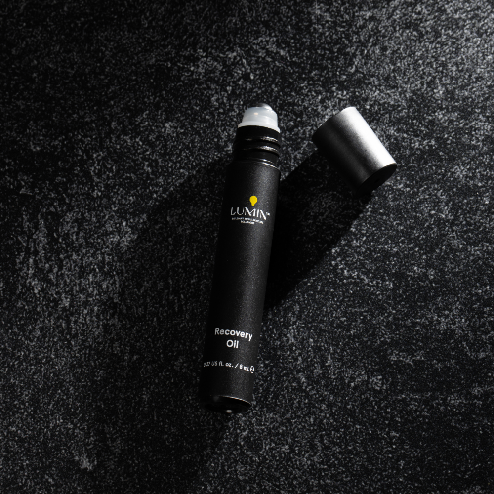 Lumin men's Recovery Oil roller bottle with black cap on textured dark surface, 0.27 fl oz skincare product