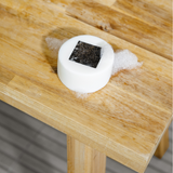 Round white soap bar with a black square center and foam bubbles on a wooden table surface.
