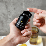 Black Lumin Anti-Redness Defense Cream container being held with a small amount of white cream on fingertip, men's skincare product.