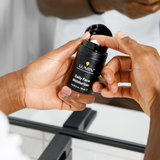 Hands applying Lumin Daily Face Moisturizer cream from black 50ml container in bathroom mirror reflection.