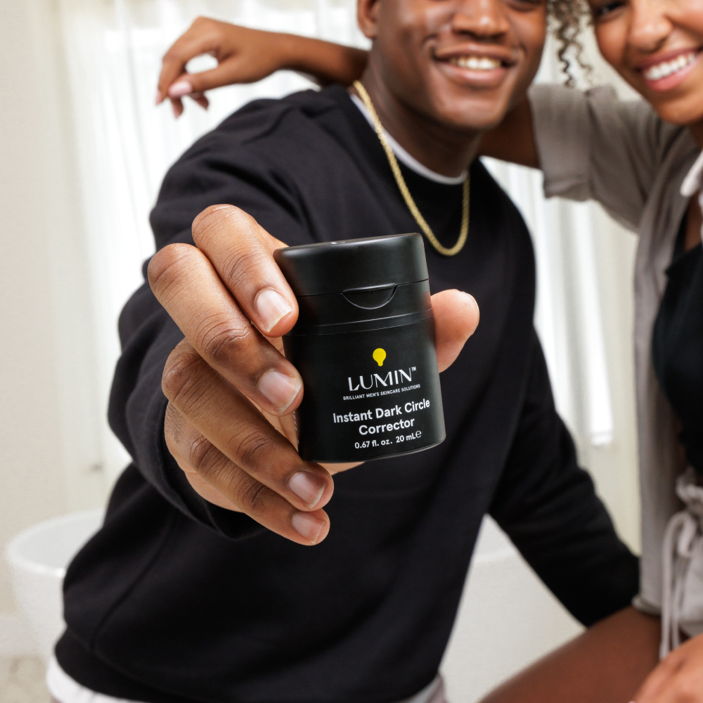 Lumin Instant Dark Circle Corrector for men held by smiling man in black shirt, promoting skincare and dark circle treatment product.