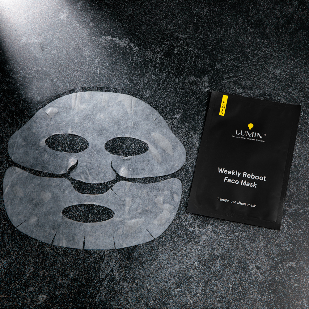 Lumin Weekly Reboot single-use men's skincare sheet face mask with eye, nose, and mouth cutouts on dark textured surface.