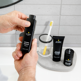 Lumin Wrinkle Defense Serum held by a man with Charcoal Face Wash, Daily Face Moisturizer, and toothbrush on bathroom counter.