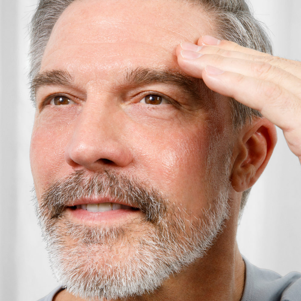 Mature man with gray beard gently touching forehead, showcasing skincare or anti-aging facial treatment for men.